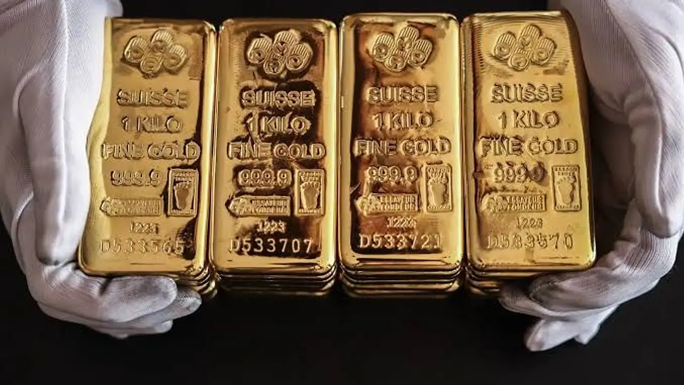 Four one-kilogram fine gold bars held in white cotton gloves